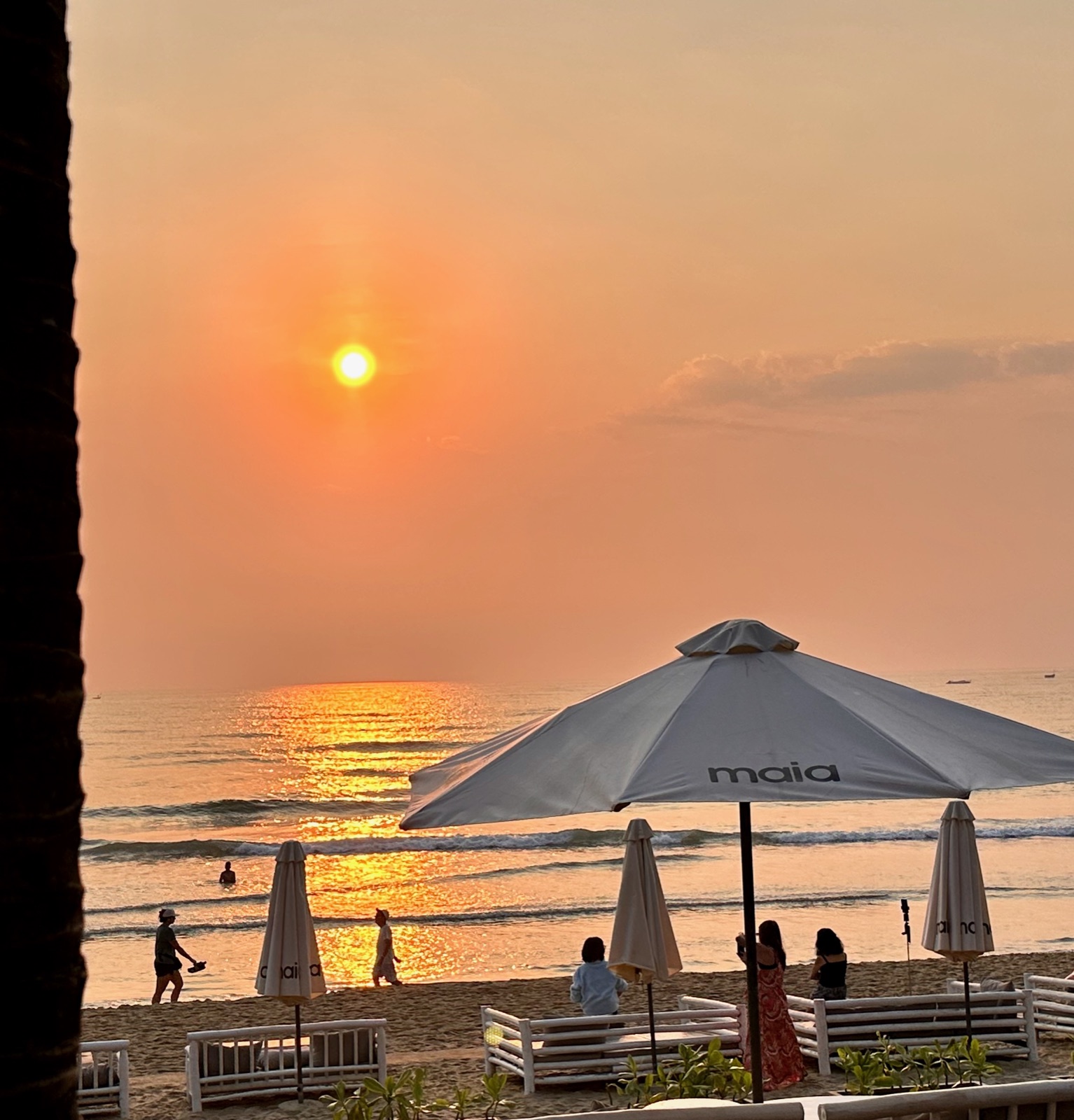 Beachgoers and umbrellas silhouetted against an orange sunrise at My An Beach